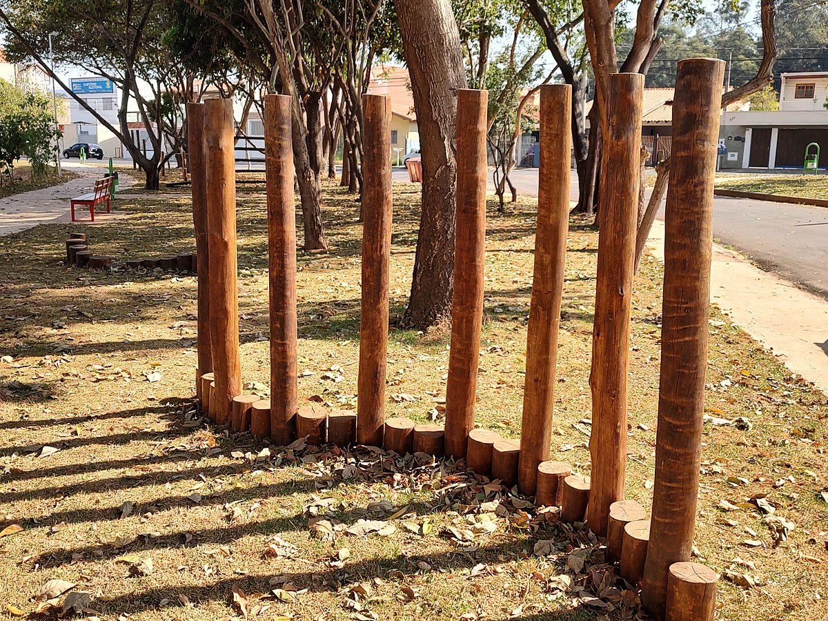 Toras roliças de eucalipto tratado de alturas diferentes fixadas no chão de uma praça, formando um circuito de equilíbrio