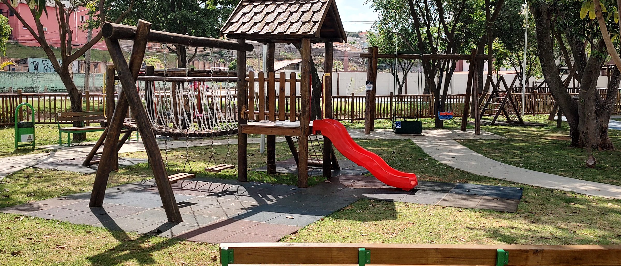 Playground de madeira com bancos em praça arborizada